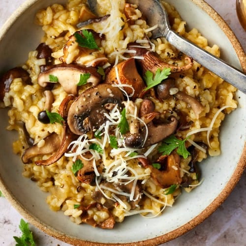 A bowl of creamy mushroom risotto with browned mixed mushrooms and parsley
